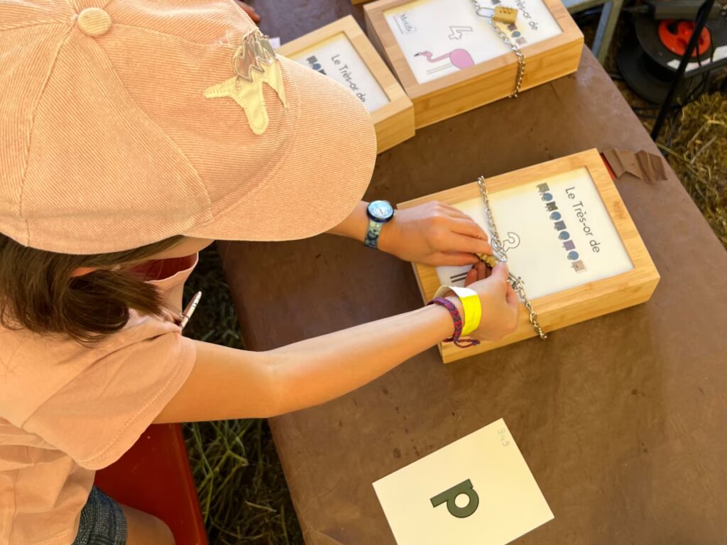 Une fillette essaie d'ouvrir un coffre avec un cadenas. Sur la table, une lettre p couleur vert poire